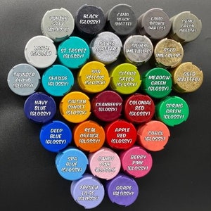 May include: Assortment of paint caps in various colors, including black, white, red, green, blue, yellow, orange, pink, and purple. Each cap has a different color and a name printed on it, such as "Winter Grey", "Black (Glossy)", "St. Tropez (Glossy)", "Sun Yellow (Glossy)", "Navy Blue (Glossy)", "Deep Blue (Glossy)", "Spa Blue (Glossy)", "French Lilac (Glossy)", and "Grape (Glossy)".