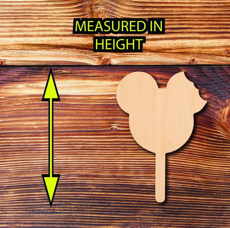 May include: A light-colored wooden Mickey Mouse-shaped cutout on a stick, with a bite taken out of the ear. The text "MEASURED IN HEIGHT" is above the cutout. The background is a dark brown wooden surface.