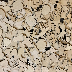 May include: A collection of various unfinished wooden cutouts, including shapes of characters, symbols, and objects. The cutouts are in a natural wood color and appear to be laser-cut. The shapes are scattered across the surface, creating a textured and layered effect.