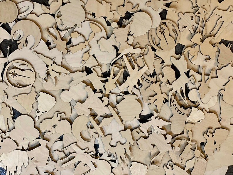 May include: A collection of various unfinished wooden cutouts, including shapes of characters, symbols, and objects. The cutouts are in a natural wood color and appear to be laser-cut. The shapes are scattered across the surface, creating a textured and layered effect.