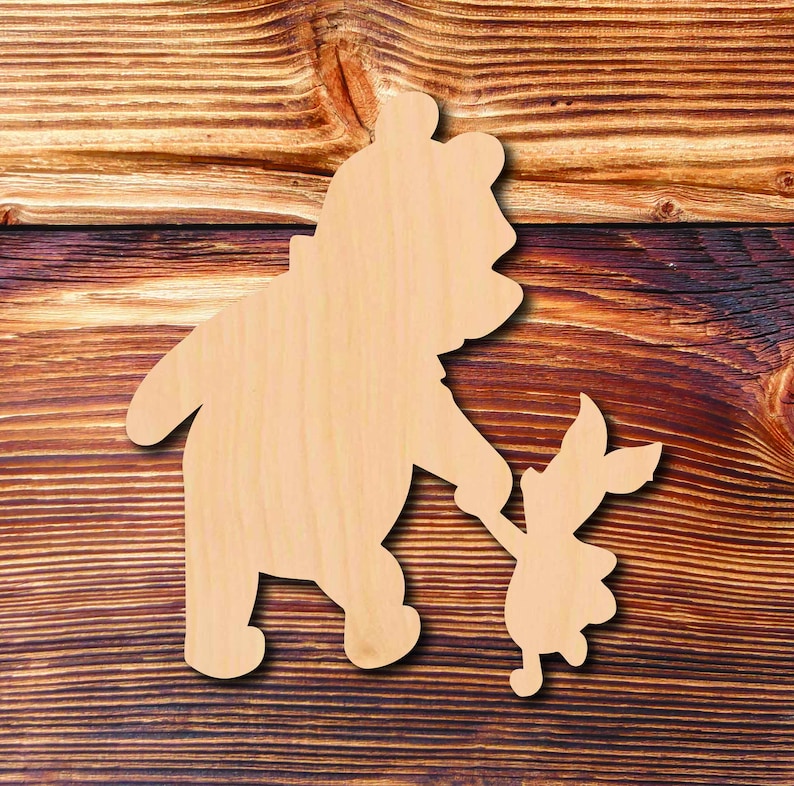 May include: Wooden cutout of Winnie the Pooh and Piglet holding hands. The cutout is a light brown color and is set against a brown wood background.