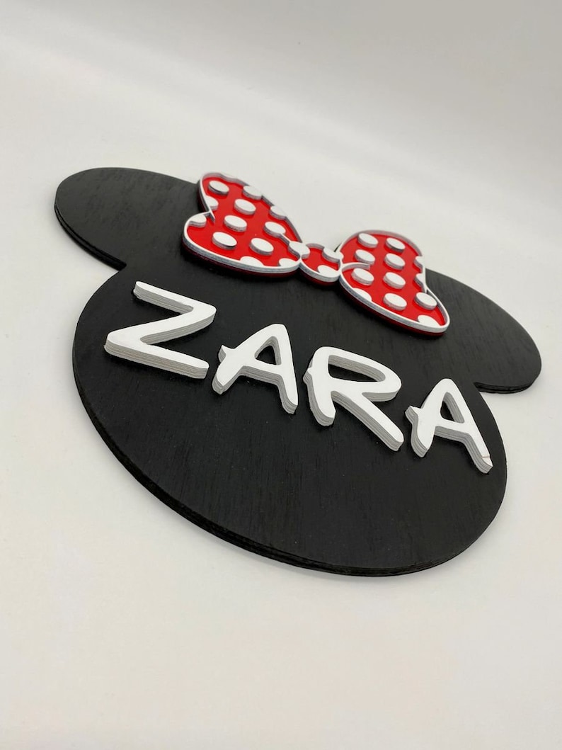 May include: Black wooden sign shaped like Mickey Mouse ears with a red bow with white polka dots and the name "ZARA" in white raised letters.