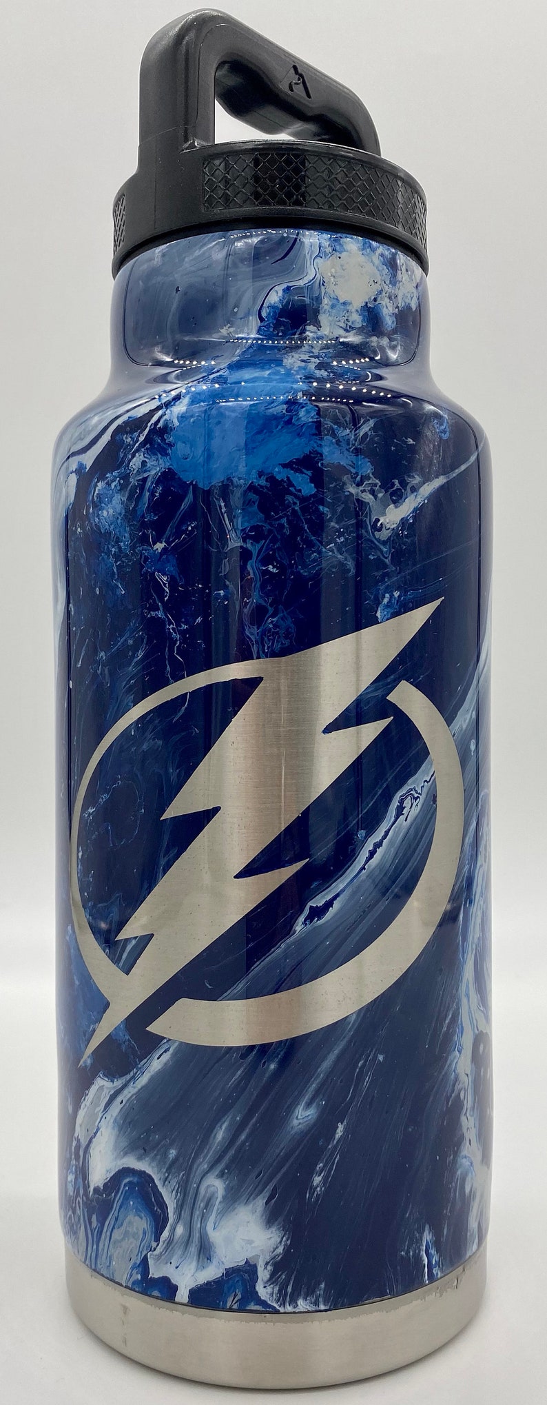 May include: A stainless steel water bottle with a black handle and a blue and white marbled design. The bottle has a silver lightning bolt logo on the front.