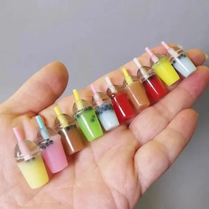 Op de afbeelding: Een verzameling van tien miniatuur bubble tea bedels in diverse kleuren zoals geel, roze, bruin, groen, wit, rood en lichtblauw. Elk klein plastic bekertje is voorzien van een doorzichtig deksel, een gekleurd rietje en donkere parels.