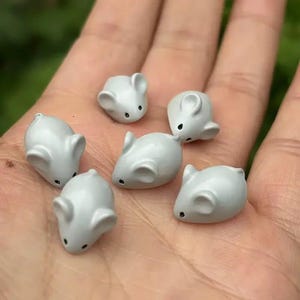 May include: Six small, light gray mouse-shaped figurines with smooth surfaces, rounded ears, and tiny black painted eyes. Each miniature mouse is sculpted in a simple, solid form, displaying a uniform matte finish across their rounded bodies.