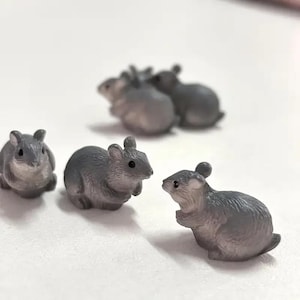 May include: A collection of five small, grey, rodent-shaped figurines. Each miniature figure features a textured surface, pointed ears, a rounded body, and small black eyes. The figures are arranged in a group, with some facing forward and others in profile, showcasing their detailed, sculpted forms.