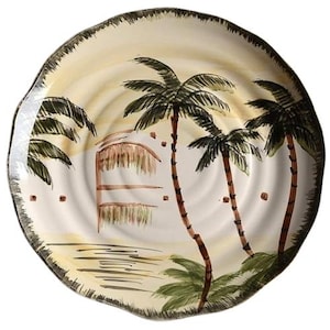 May include: A round ceramic plate with a hand-painted tropical scene. The design features palm trees, a hut, and a beach landscape in shades of green, brown, and yellow. The plate has a wavy, textured rim.