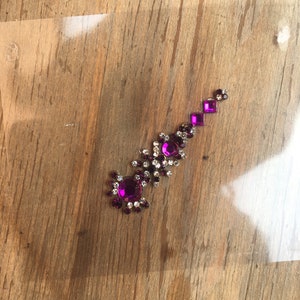 May include: A purple and clear rhinestone body jewel with a flower design.