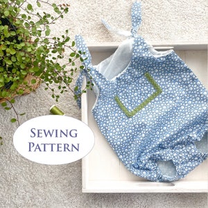 May include: A blue and white floral print baby romper with green trim and tie straps. The romper is displayed on a white tray with the text "SEWING PATTERN" in a white oval.