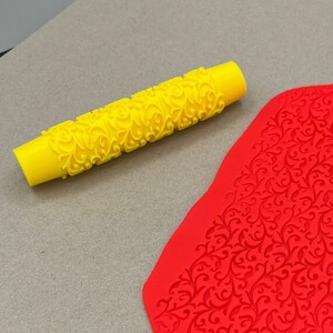 May include: A yellow rolling pin with a decorative pattern and a red sheet of fondant with a matching pattern.