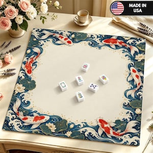 May include: A square game mat featuring a cream-colored center and a border decorated with red and white koi fish, dark blue stylized waves, and lotus flowers. Six white rectangular mahjong tiles are scattered in the center.