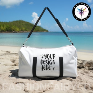 May include: White travel duffel bag with black straps and the text "YOUR DESIGN HERE" printed on the front. The bag is sitting on a sandy beach.