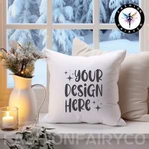 Puede incluir: Almohada blanca con el texto "YOUR DESIGN HERE" en letras grises con pequeños detalles de brillo. La almohada está sentada en un alféizar de ventana blanco con un jarrón de vegetación y una vela en primer plano.
