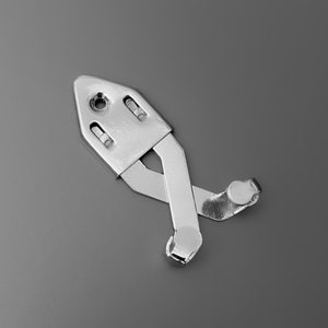 Op de afbeelding: Een zilverkleurig metalen kastdeur scharnier met een veermechanisme. Het scharnier is in gesloten positie.