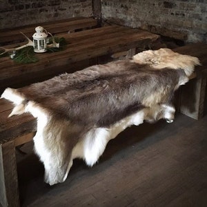 May include: A brown and white reindeer hide rug draped over a wooden table. The rug is soft and fluffy, with a natural look.
