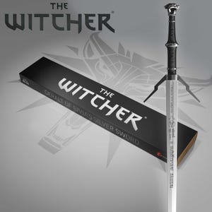 Pode incluir: Uma espada prateada com punho preto e pomo decorativo, ao lado de uma caixa preta. A caixa e a espada estão rotuladas com "The Witcher" e "Geralt of Rivia's Silver Sword". O fundo é cinza.