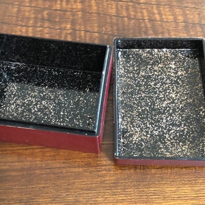 May include: Two empty, square, red boxes with black interiors. The interiors have a speckled, gold-flecked finish.