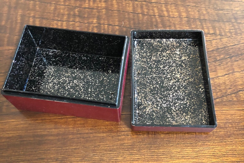 May include: Two empty, square, red boxes with black interiors. The interiors have a speckled, gold-flecked finish.