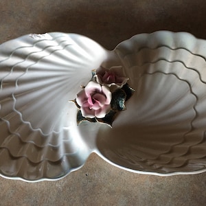 Puede incluir: Un plato de servir de cerámica blanca con forma de dos conchas con un diseño en relieve de rosas rosas en el centro.