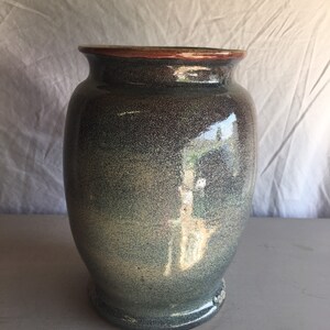 以下が含まれることがあります： 斑点のある青と灰色の釉薬をかけた陶器の花瓶。花瓶は丸みを帯びたボディとわずかに広がった縁を持っています。縁は薄い赤褐色の釉薬の帯でアクセントが付けられています。