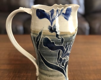 May include: A white ceramic pitcher with a blue and gray floral design. The pitcher has a wide mouth and a handle.