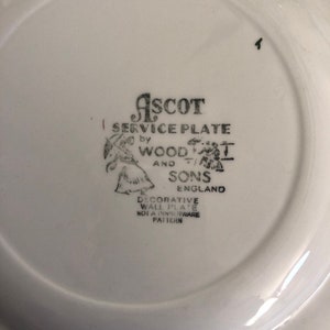 May include: A white ceramic plate with a black and white image of a woman and a man holding umbrellas. The text "ASCOT SERVICE PLATE by WOOD AND SONS ENGLAND DECORATIVE WALL PLATE NOT A DINNERWARE PATTERN" is printed on the plate.