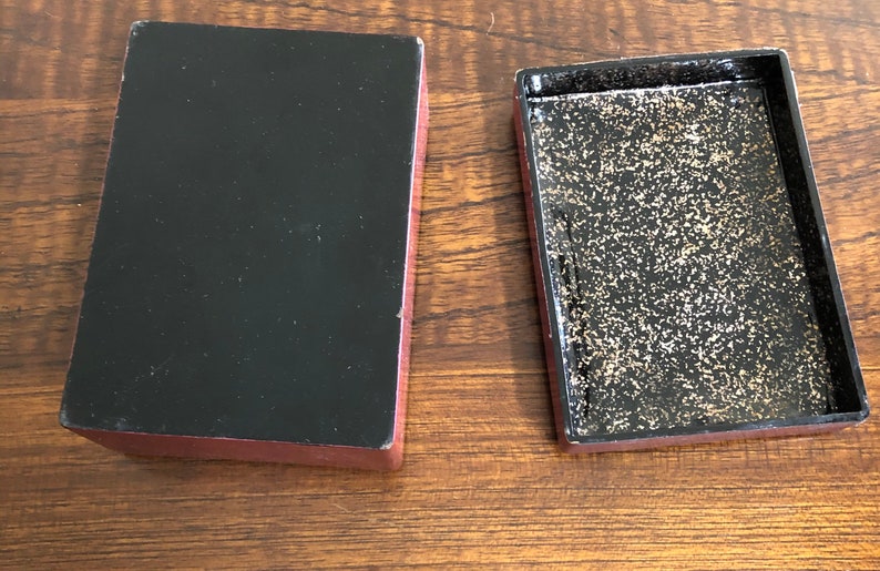 May include: A red wooden box with a black interior. The box is open and the inside is lined with gold glitter.