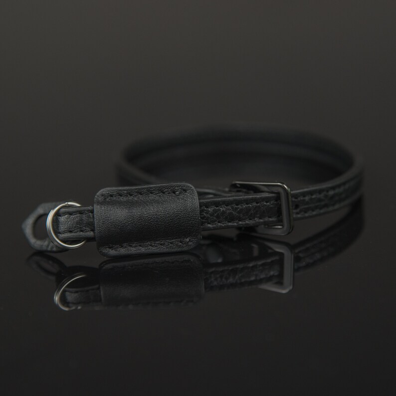 Puede incluir: Una correa de c&aacute;mara de cuero negro con una hebilla de metal y un peque&ntilde;o lazo de cuero. La correa est&aacute; dise&ntilde;ada para usarse alrededor del cuello o la mu&ntilde;eca.
