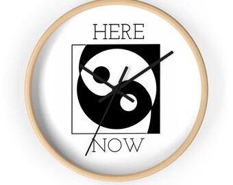 Puede incluir: Un reloj redondo con marco de madera y una cara blanca. La cara del reloj presenta un símbolo yin yang en blanco y negro con las palabras "HERE NOW" impresas debajo.
