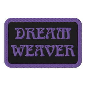Pode incluir: Etiqueta bordada roxa com fundo preto e o texto "DREAM WEAVER" em uma fonte estilizada.
