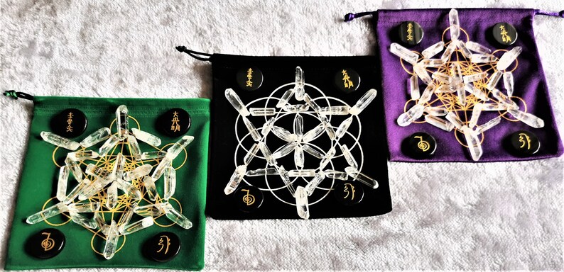 May include: Three velvet pouches with drawstring closures, each containing a set of clear quartz crystal points arranged in a geometric pattern. The pouches are green, black, and purple. Each pouch has black circular stones with gold lettering.