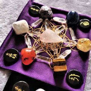 Könnte beinhalten: Ein violetter Samtbeutel mit einem goldenen geometrischen Muster und verschiedenen Kristallen und Steinen, darunter klarer Quarz, Rosenquarz, Tigerauge, Karneol, Citrin, Amethyst und schwarzer Obsidian. Der Beutel enthält auch schwarze runde Steine mit goldenen Symbolen.