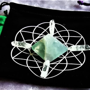 May include: Three velvet pouches with a green, black, and purple exterior. Each pouch contains a clear crystal pyramid and four clear quartz points arranged in a star pattern.