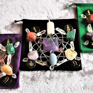 May include: Three velvet pouches with black lining, each containing a crystal grid set with various crystals, including amethyst, clear quartz, rose quartz, and citrine. Each pouch also includes a white candle and black stones with gold symbols.