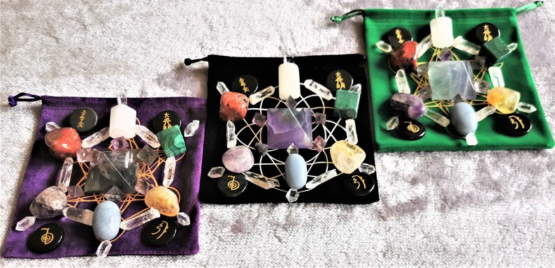 May include: Three velvet pouches with black lining, each containing a crystal grid set with various crystals, including amethyst, clear quartz, rose quartz, and citrine. Each pouch also includes a white candle and black stones with gold symbols.