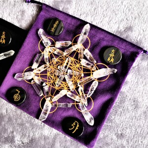 May include: A purple velvet pouch with a gold geometric pattern and clear quartz crystals. There are four black circular stones with Japanese characters on them.