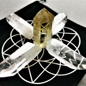 May include: Four clear quartz crystal points and one yellow citrine point arranged in a star pattern on a black fabric with a white geometric design.