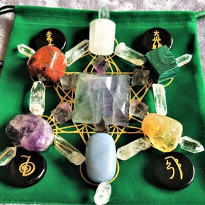 May include: A green velvet pouch with a gold geometric pattern and various crystals and stones, including clear quartz, amethyst, citrine, red jasper, malachite, fluorite, and selenite. There are also black circular stones with symbols on them.
