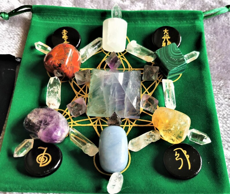May include: A green velvet pouch with a gold geometric pattern and various crystals and stones, including clear quartz, amethyst, citrine, red jasper, malachite, fluorite, and selenite. There are also black circular stones with symbols on them.