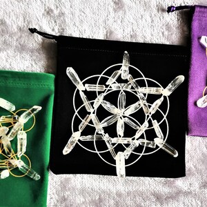 May include: Three velvet pouches with different colored linings, each containing a crystal grid made of clear quartz points. The grids are arranged in a geometric pattern, with a gold wire frame.