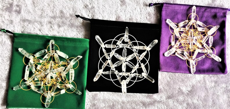 May include: Three velvet pouches with different colored linings, each containing a crystal grid made of clear quartz points. The grids are arranged in a geometric pattern, with a gold wire frame.