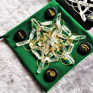 May include: A green velvet pouch with a gold geometric pattern and clear quartz points. There are five black wooden tokens with gold symbols on them.