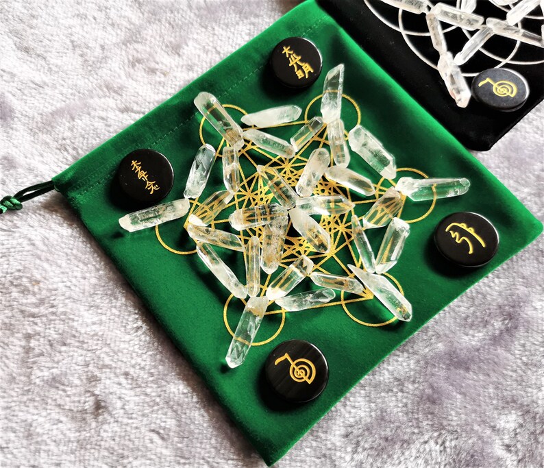 May include: A green velvet pouch with a gold geometric pattern and clear quartz points. There are five black wooden tokens with gold symbols on them.
