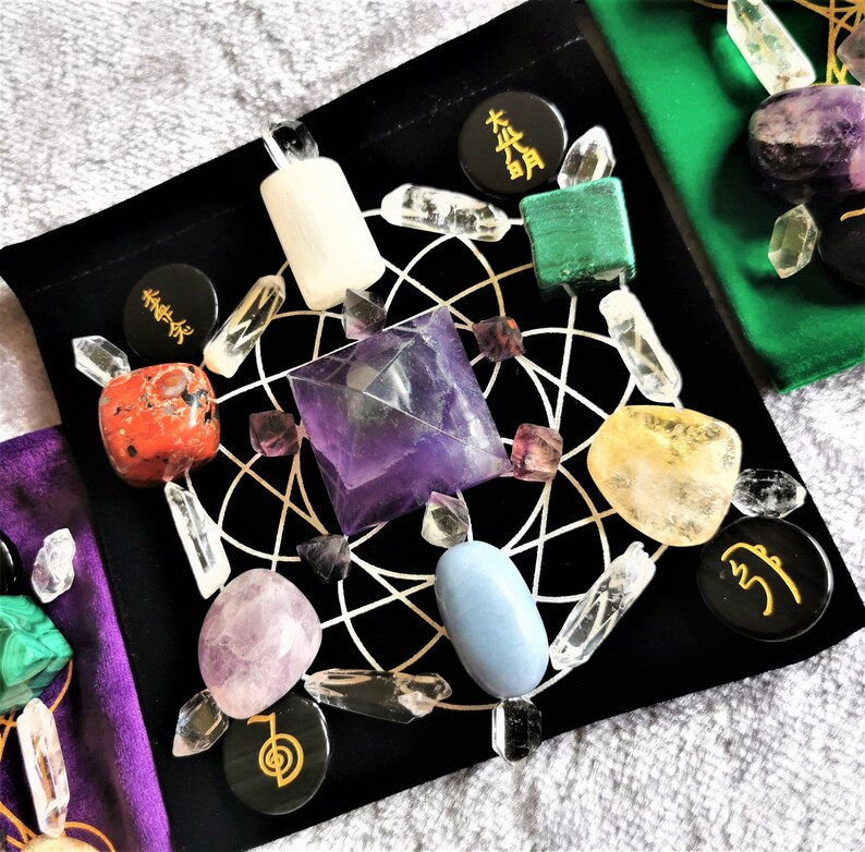 May include: A black velvet pouch with a crystal grid and various crystals, including amethyst, clear quartz, rose quartz, and citrine. The pouch also includes black stones with gold lettering, including "木" and "火".