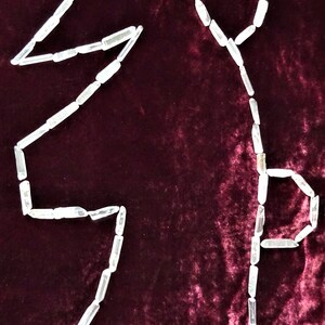 May include: A white crystal quartz is arranged in the shape of a letter "S" on a dark red velvet background.