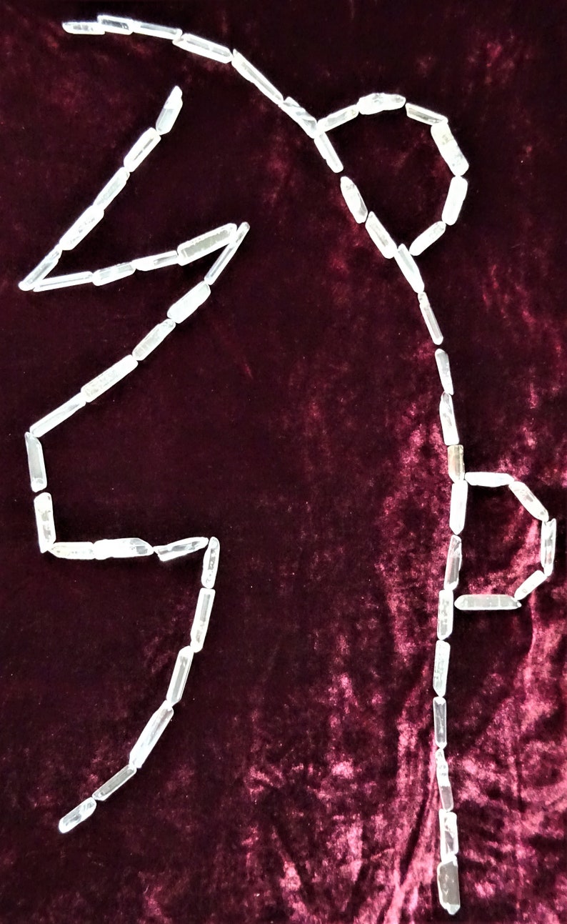 May include: A white crystal quartz is arranged in the shape of a letter "S" on a dark red velvet background.