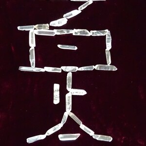 May include: The Chinese character for "stone" is spelled out using clear quartz crystals on a dark red velvet background.