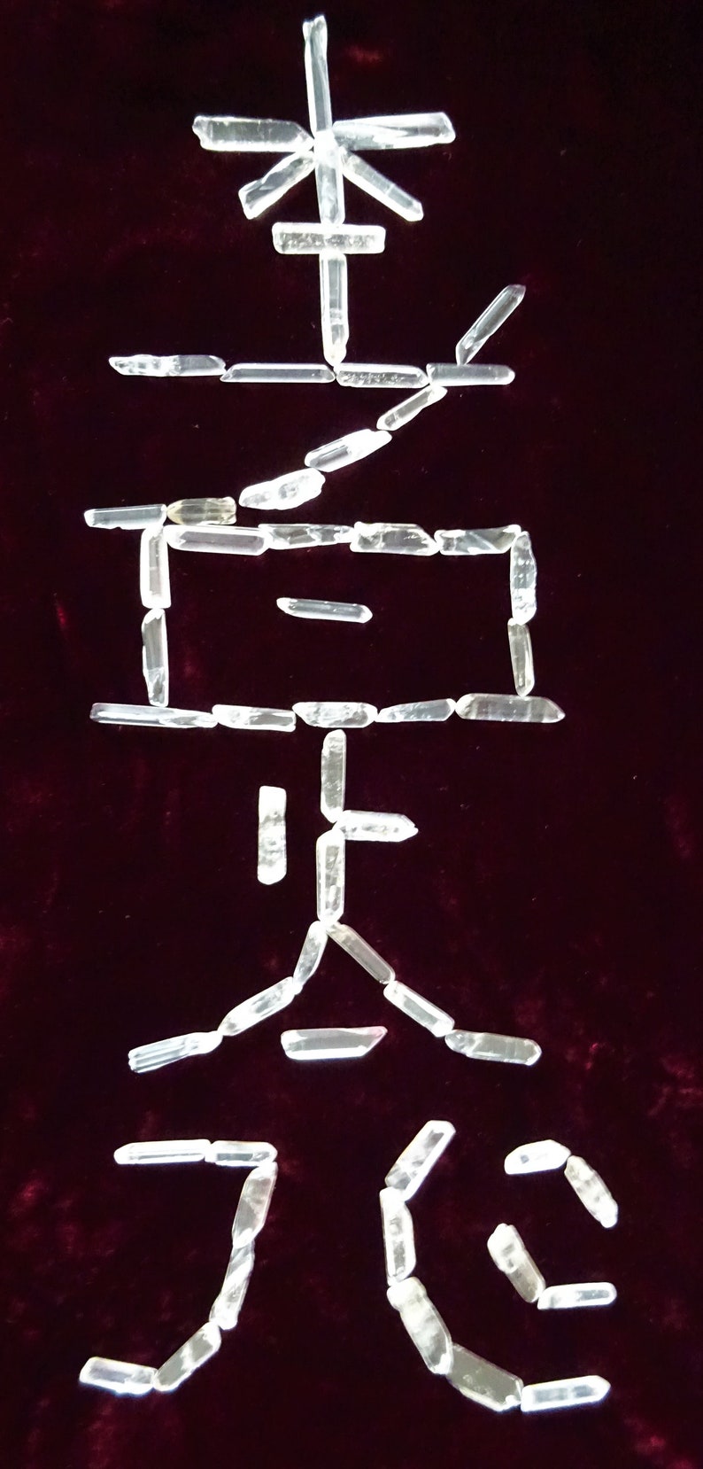 May include: The Chinese character for "stone" is spelled out using clear quartz crystals on a dark red velvet background.