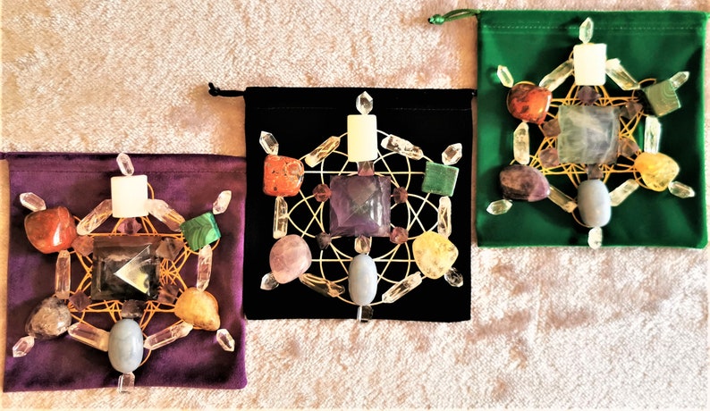 May include: Three velvet pouches with a crystal grid inside each. The pouches are green, black, and purple. The crystal grids are made of clear quartz crystals, amethyst, rose quartz, citrine, carnelian, and other crystals.