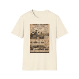 Puede incluir: Una camiseta de manga corta color crema con un estampado gráfico de estilo vintage titulado The Grand Encampment Mining Project. El diseño incluye ilustraciones detalladas de infraestructura minera, teleféricos y texto con datos históricos.